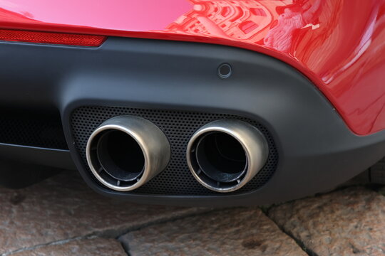 A detail of the rear section of an iconic red Italian sports car highlighting its distinctive twin exhaust outlets and the glossy paintwork, sculpted bodywork and refined performance