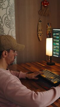 A man sits comfortably at home working on a computer and editing video footage. The scene shows a modern creative workflow with video editing software, timeline adjustments