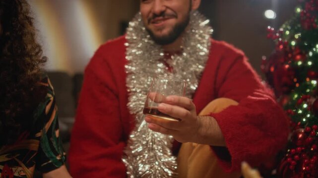 Young biracial man holding drink glass and eating pizza during Christmas celebration with friends. Footage suitable for holiday party ads, beverage marketing, and food delivery campaigns