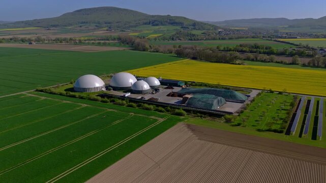 Aerial video of a modern biogas facility and neighboring solar installation surrounded by extensive agricultural fields and rolling countryside in Germany.