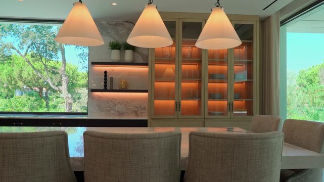 Elegant and modern dining room showcasing a marble table. Stylish chairs. And designer pendant lights. With large windows opening to a lush green garden for a perfect indoor outdoor living experience