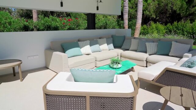 Modern luxury villa outdoor lounge with comfortable sofa, armchairs and cushions on a sunny patio overlooking a lush tropical gardenperfect for relaxing, summer leisure and entertaining