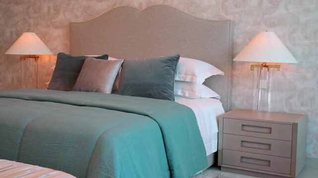 Smooth camera movement revealing a stylishly decorated master bedroom in a luxury home or hotel, showcasing the king size bed with turquoise bedding, elegant bedside lamps, and modern furniture