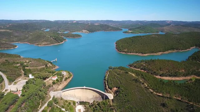 Expansive aerial perspective showing the bravura dam, a large concrete arch gravity structure holding back the turquoise waters of the odeaxere river reservoir in the algarve region of portugal