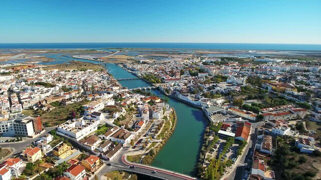 Panoramic aerial footage flying over the gilao river, revealing the historic town of tavira, the ancient roman bridge, and the beautiful algarve coastline under a clear blue sky in portugal