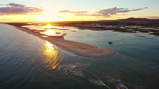 Stunning aerial view of a dredging boat working near a sand spit in ria formosa natural park at fuseta, algarve, portugal, with a beautiful golden sunset reflecting on the calm ocean water