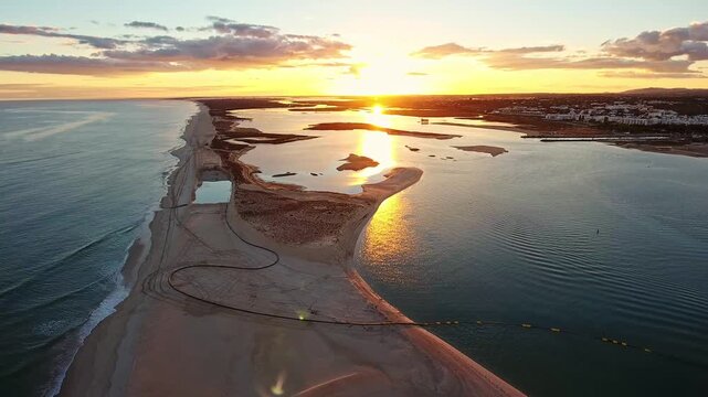 Stunning aerial perspective showing the sunset over the ria formosa natural park in fuseta, with golden light reflecting on the water, sandbanks, and the distant town of tavira, portugal