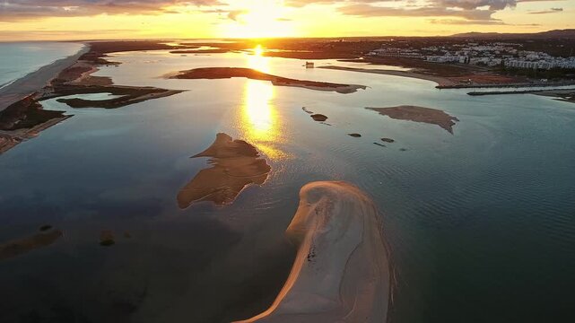 Stunning aerial view of the sun rising over the sandbanks and calm waters of the ria formosa natural park lagoon in fuseta, with the golden sunlight beautifully reflecting on the surface
