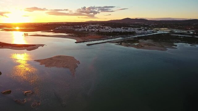 Beautiful golden sun setting over the coastal town of fuseta in the algarve, with the calm waters of the lagoon reflecting the warm light and showcasing the stunning natural landscape of portugal