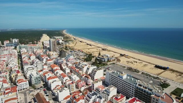 Drone view flying over the coastal city of monte gordo in the algarve region of southern portugal, showing beautiful architecture, a vast sandy beach, and the blue atlantic ocean on a sunny day