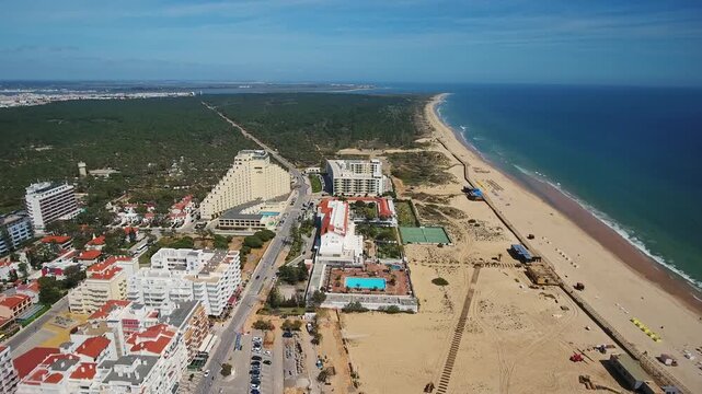 High altitude aerial view flying over the resort town of monte gordo, showcasing the expansive sandy beach, atlantic ocean coastline, and modern hotels on a sunny day in algarve, portugal