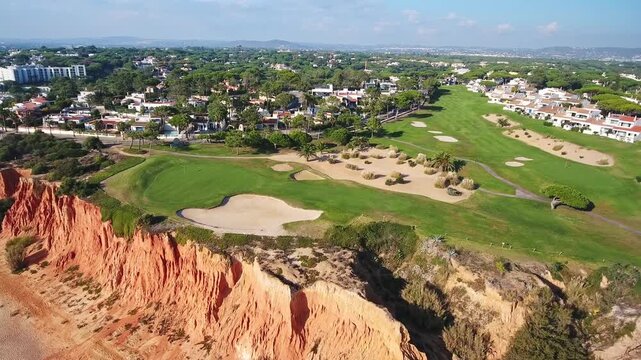 Stunning aerial view of lush green golf course atop red cliffs at vale do lobo, algarve, overlooking the atlantic with beach, fairways, villas and dramatic coastal scenery
