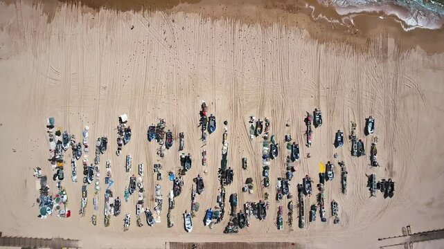 Zenithal aerial view showing traditional fishing boats resting on the sandy beach of monte gordo in the algarve, with fishermen and their equipment organized between two small wooden piers