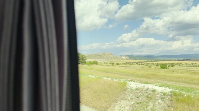 A vehicle window frames the passing landscape. Green fields and hills glide by under a calm blue sky. This peaceful journey through Crimea feels truly wonderful and free.