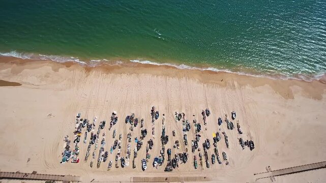 Aerial drone view moving backwards from traditional fishing boats parked on the golden sand of monte gordo beach in algarve, portugal, showing the vibrant green and blue ocean waves