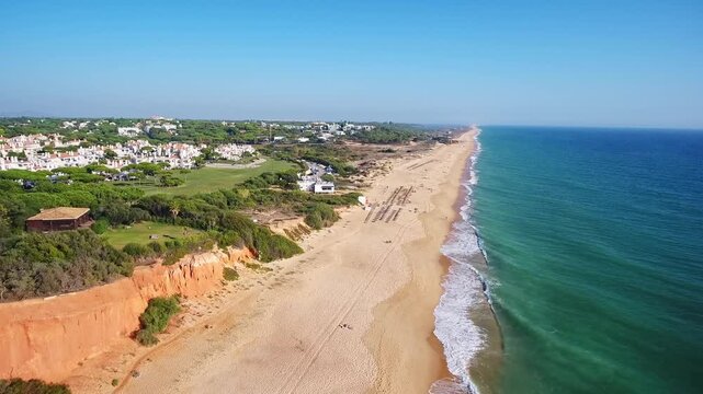 Aerial footage of the beautiful praia de garrao beach, revealing the stunning red cliffs, golden sand, and turquoise atlantic ocean waters meeting the coastline in vale de lobo, algarve