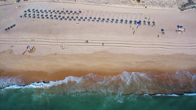 Majestic top down aerial perspective showing beautiful turquoise ocean waves breaking on a sandy beach with tourists enjoying a sunny day, creating a serene and relaxing summer vacation scene