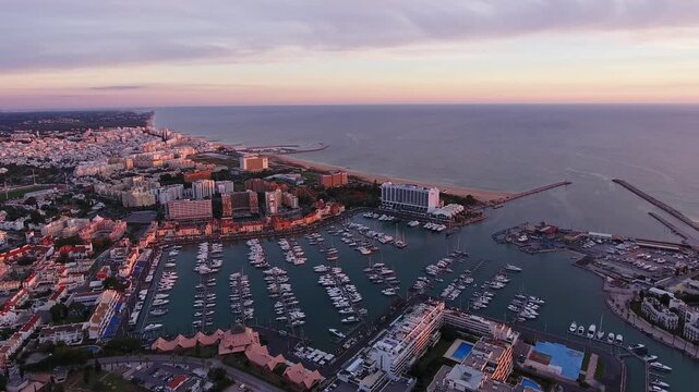 Picturesque aerial view revealing the beautiful vilamoura marina and the city skyline along the algarve coast, with moored yachts and boats illuminated by the warm light of a colorful sunset