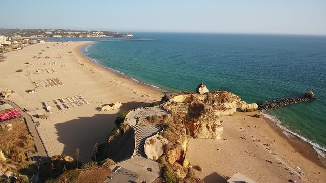Stunning aerial view slowly revealing praia da rochas golden sand, turquoise atlantic waters and dramatic cliffs with a scenic viewpoint above portimaos sunlit algarve coastline