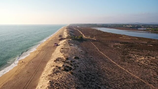Aerial drone shot showing the stunning coastline of quinta do lago in the algarve, portugal, featuring a vast sandy beach next to the calm waters of the ria formosa natural park at sunset