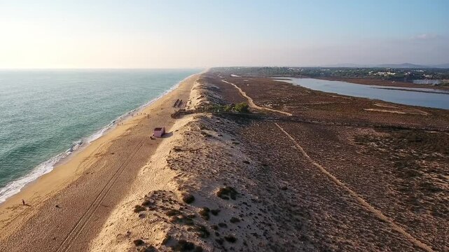 Dramatic aerial perspective flying over the extensive sand dunes of quinta do lago beach, revealing the atlantic ocean on one side and the ria formosa lagoon on the other, at sunset in portugal