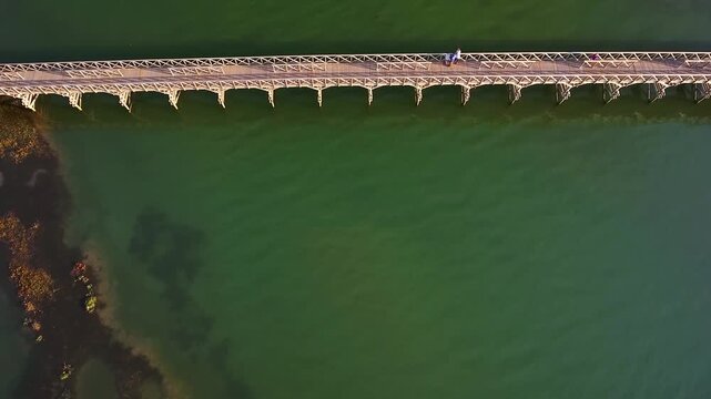 Majestic aerial top down view showing a wooden pedestrian bridge crossing a beautiful green lagoon in the algarve region of portugal, a famous destination for luxury golf courses and resorts