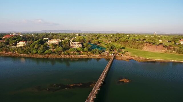 Aerial view of the long wooden pedestrian bridge in quinta do lago, algarve, connecting a luxury resort and a golf course across the ria formosa lagoon with people walking during a sunny day