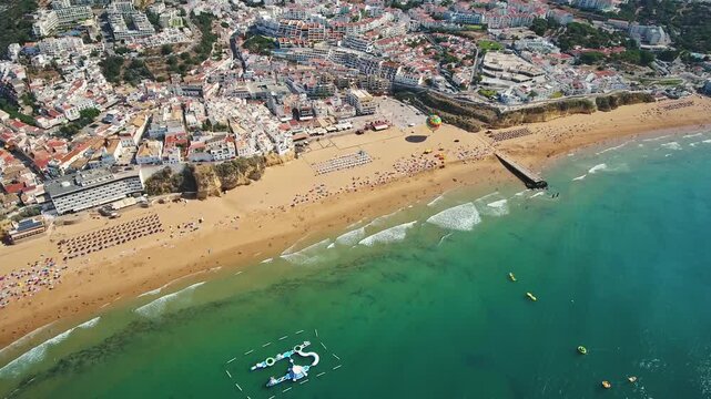 Panoramic aerial footage showing the beautiful albufeira old town and the crowded fishermen's beach - praia dos pescadores - in the famous algarve region of portugal, a top summer destination