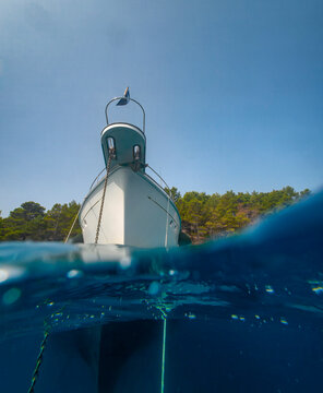 Luxury yacht bow and anchor chain seen from a split level underwater perspective, with clear blue sea, sunny sky and open space for nautical travel concepts