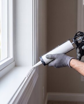 Hand applies caulk sealant along window frame with caulking gun