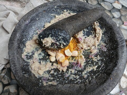 Freshly ground herbs and spices in a traditional stone mortar and pestle (cobek dan ulekan) for authentic Indonesian cooking preparation