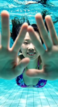 Young woman swimming underwater in clear blue swimming pool smiling at camera.