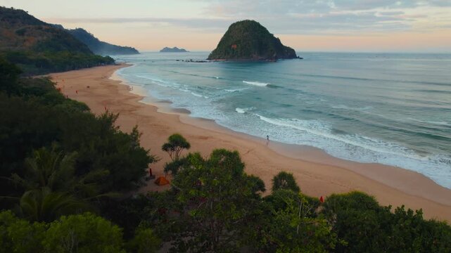Banyuwangi, East Java, Indonesia - 31 August 2026: Aerial view of Red Island Beach with its iconic rocky islet, gentle waves rolling onto the sandy shore, and lush coastal vegetation.