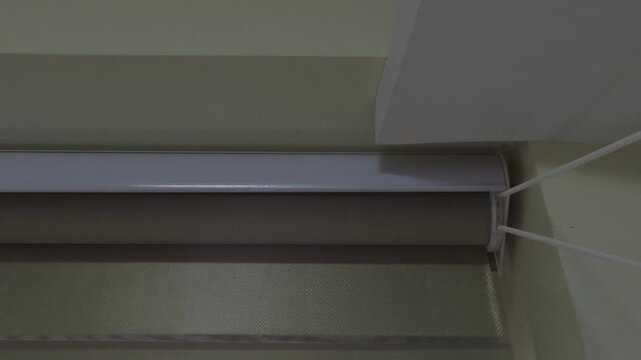 A close up of a white top casing and beaded pull chain of a modern dual layered roller blind installed within a residential window frame