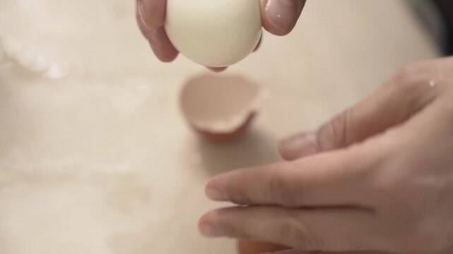 Close-up of caucasian hands peeling a brown boiled egg