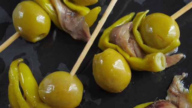 Close-up of traditional Spanish Gilda pintxos with green olives, anchovies and pickled peppers on skewers. High quality 4k footage