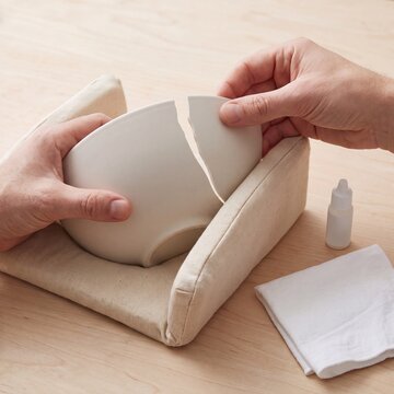 Hands aligning broken ceramic bowl pieces before repair