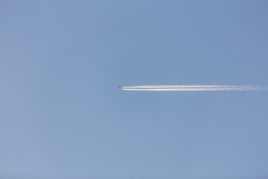 A thin white contrail from an aircraft stretches across a clear light blue sky, viewed from below.