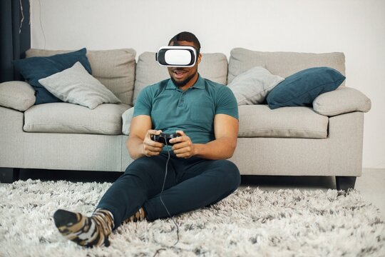 Black guy with virtual reality glasses sitting on a carpet in living room
