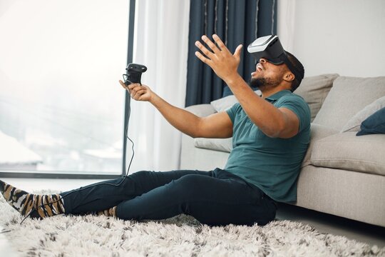 Black guy with virtual reality glasses sitting on a carpet in living room