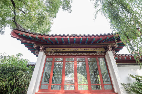A low-angle shot of a traditional Chinese pavilion with ornate lattice windows and curved tiled roof, surrounded by greenery.