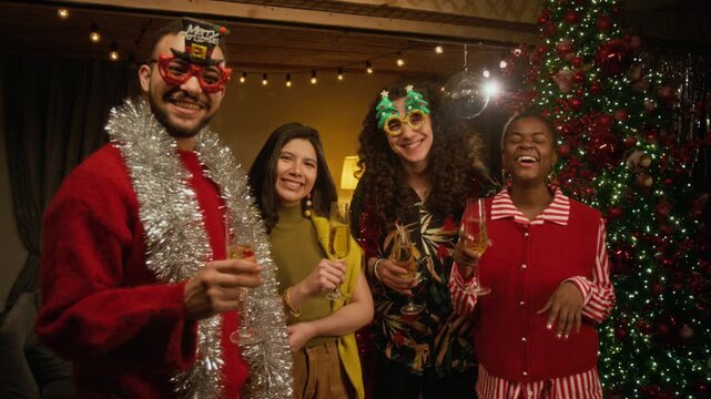 Portrait of multiethnic young friends holding champagne flutes, celebrating Christmas near decorated tree. Footage suits holiday advertising and New Year marketing campaigns