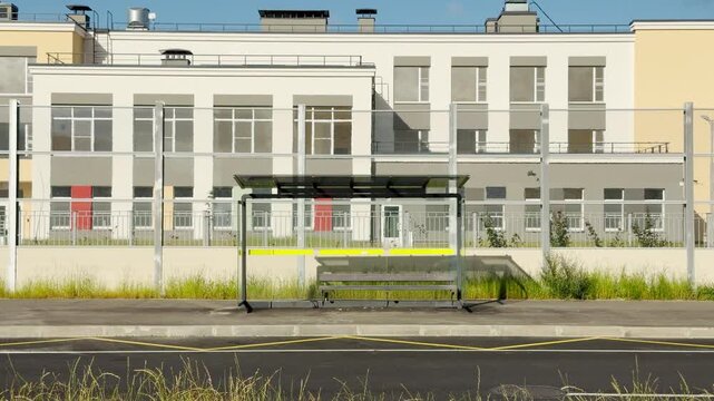 An empty bus stop stands quietly on an urban street before a modern building. This deserted scene evokes a calm, lonely, and peaceful feeling of quiet daily life.