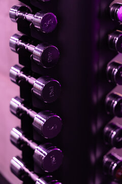 Close up view of chrome dumbbells arranged on a rack under purple ambient lighting in a modern fitness facility.