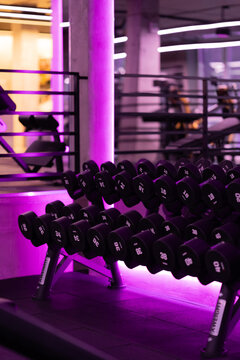 Modern gym dumbbell rack illuminated with vibrant purple lighting, creating a dramatic atmosphere for strength training and fitness workouts.