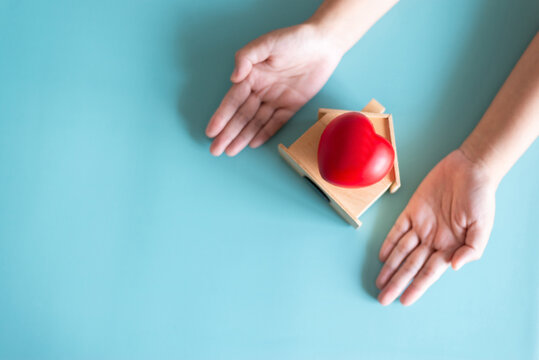 Overhead view of hands protecting wooden house model with red heart on green background