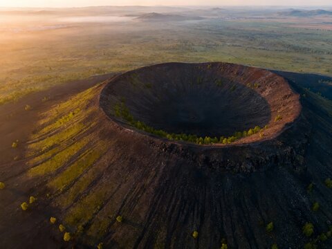Aerial view of a volcanic crater at sunrise with surrounding landscape