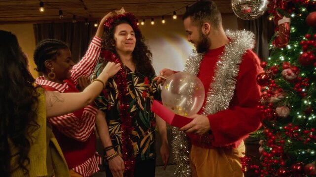 Diverse young friends playfully decorating friend with festive tinsel and Christmas ornaments. Clip suitable for holiday marketing, winter party commercials, and seasonal advertising