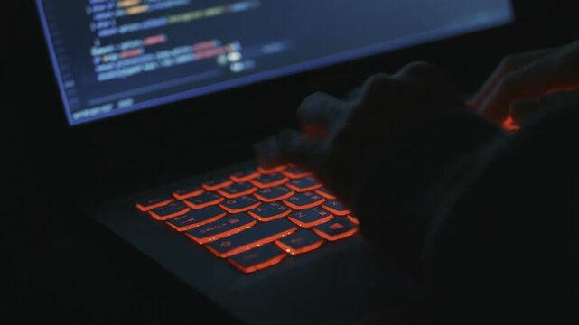 Hacker type code on laptop with red backlight in dark room for cyber security or IT background