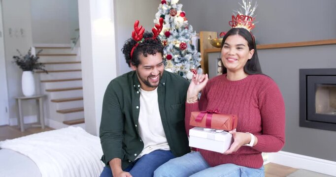 African American couple in Christmas room, woman presenting stacked gifts, man reaching surprised